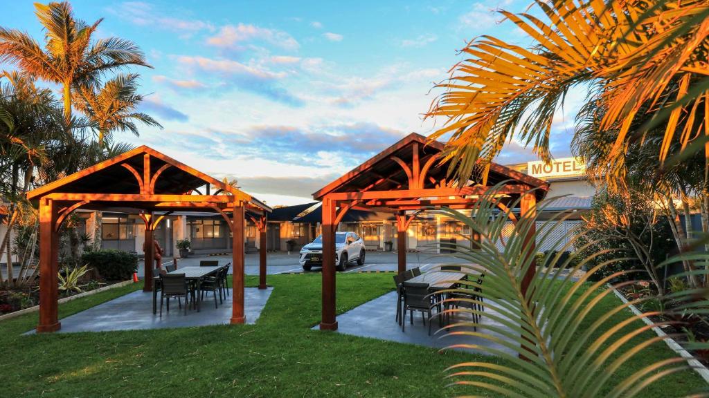 A beautiful sunset photo of a motel's common area with two dark wood gazebos, each covering an outdoor dining set.