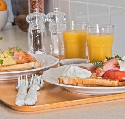 Two identical breakfast plates served on a light wooden tray in a kitchen.