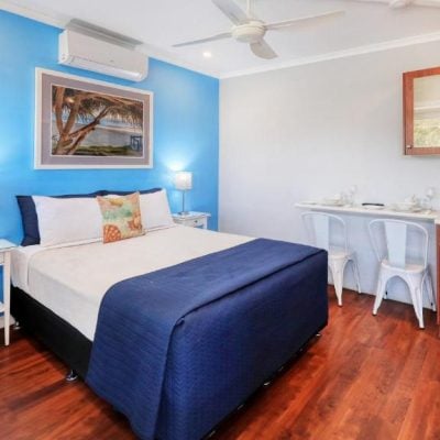 A bright motel room with a queen bed against a vibrant blue accent wall.